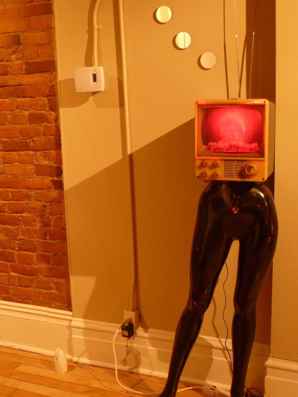 A small vintage television showing a red mushroom cloud, standing as the head on a pair of black mannequin legs