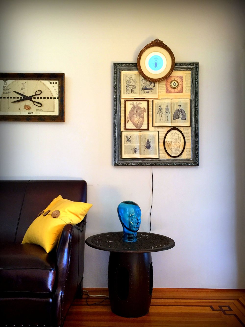 A large ornate frame of anatomical and insect engravings on open book pages, a round gilt frame with a glowing blue screen at its top, hung above a blue glass head