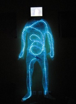 A standing figure outlined in glowing blue lights, a small screen for a head, in a dark room