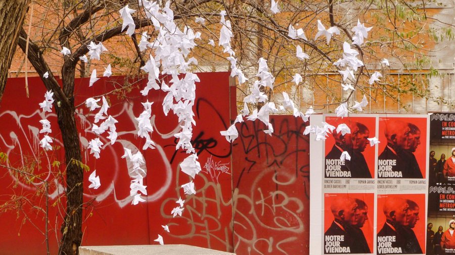 White paper birds hanging in a tree in front of a red graffiti wall